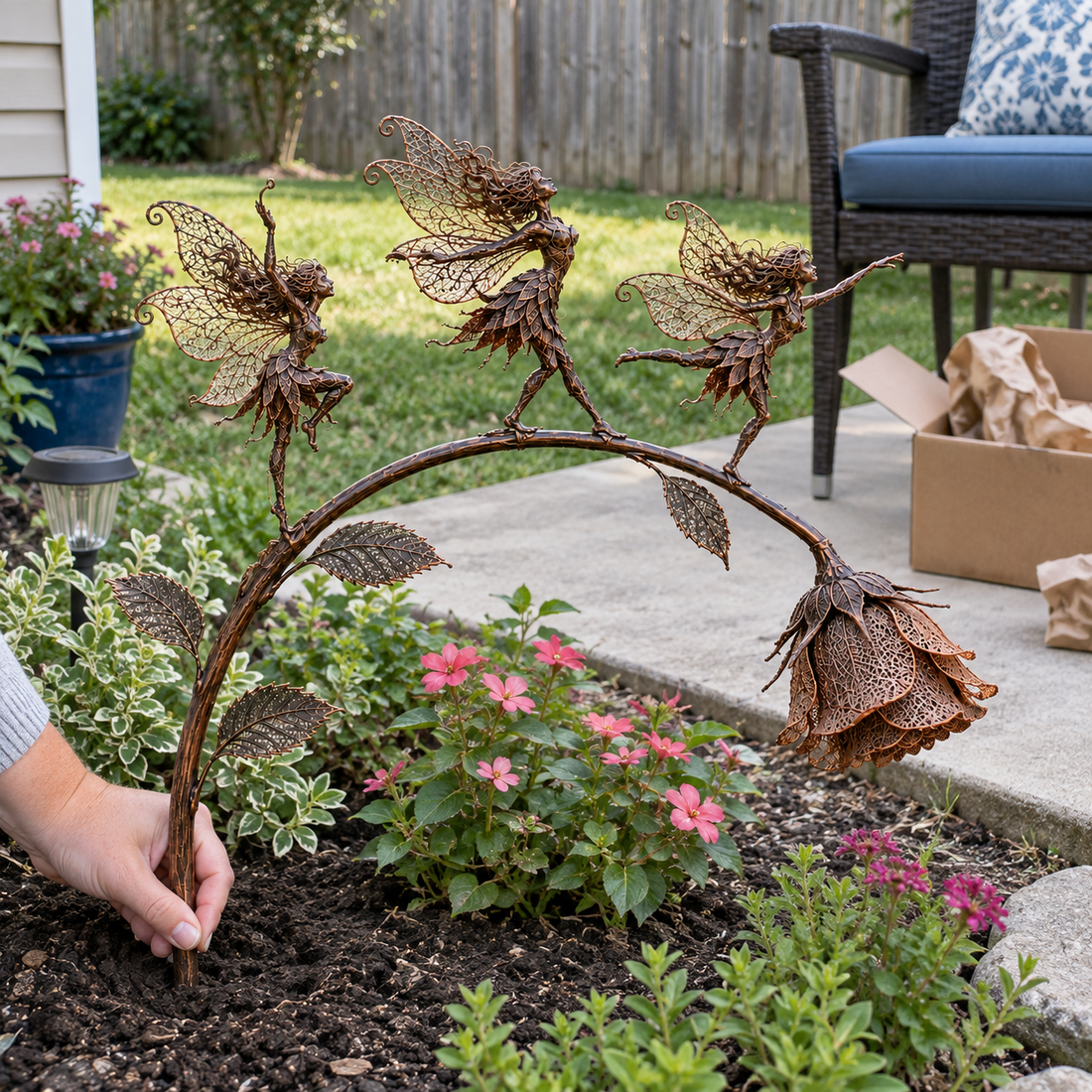 AI-generated scene of a hand steadying three rose fairies in a backyard flower bed near a patio chair